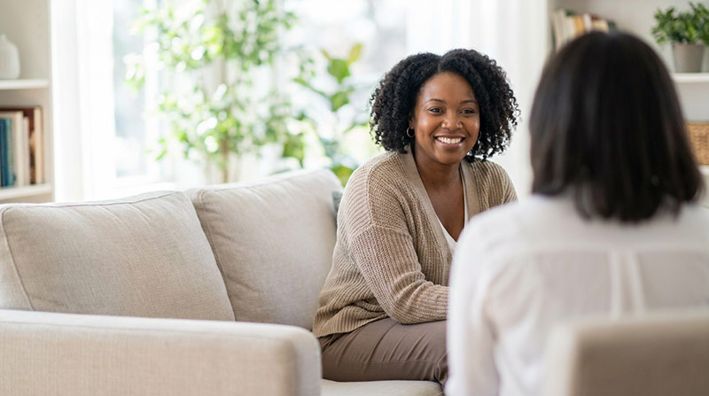 An older couple sits on a sofa at home with their adult daughter